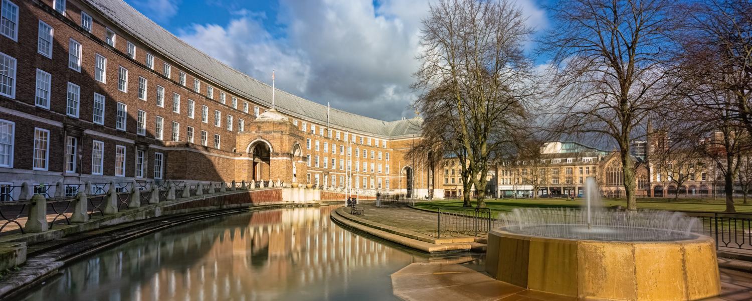 The curved brick façade, central archway, reflecting water canal and fountain of Bristol City Hall